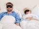 Young Couple Sleeping Comfortably On Bed Using Eye Mask