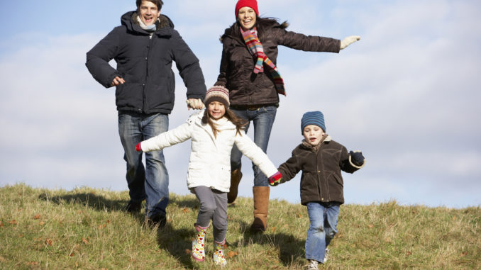 Family Running In The Park Wearing Winter Clothes