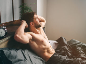Carefree guy enjoying new day. Sexy, happy bearded man in bed.