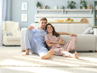 The happy couple in pajamas sitting on the floor background of the sofa in the living room.