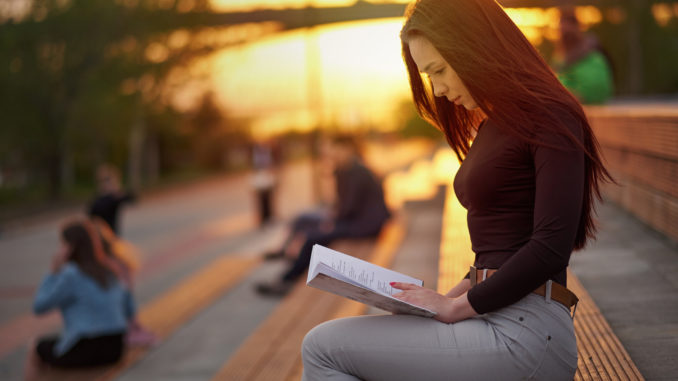 Young Asian woman reading a book in the evening at sunset. outdoor city portrait.