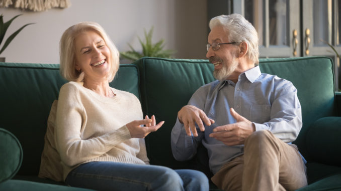 Happy carefree excited elderly family couple laughing, joking, talking, sharing good news, enjoying common weekend time in cozy living room, old people funny activities concept.