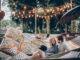 Stylish hipster couple cuddling and relaxing in hammock under retro lights in evening summer park. rustic men and women embracing and resting in forest. space for text. summer vacation