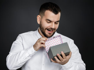 Portrait of handsome bearded man in white shirt opens gift box isolated on black background