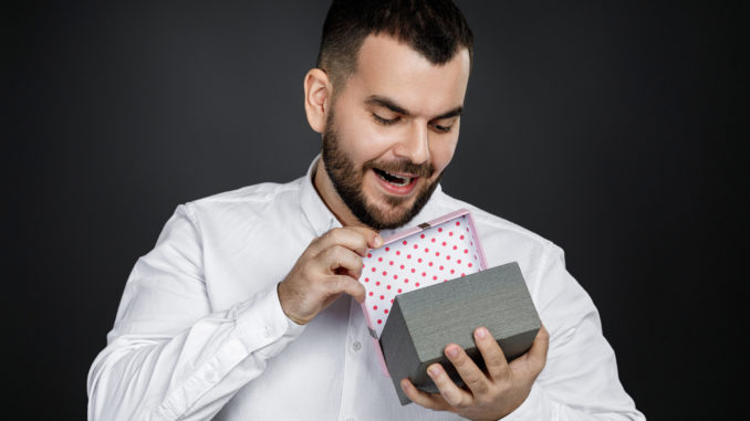 Portrait of handsome bearded man in white shirt opens gift box isolated on black background