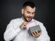 Portrait of handsome bearded man in white shirt opens gift box isolated on black background