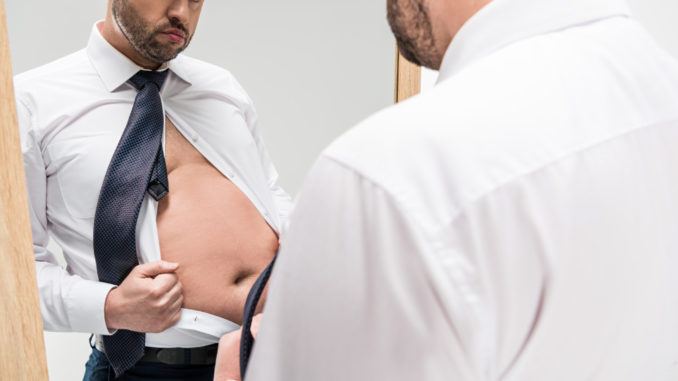 Sad overweight man in formal wear looking at mirror reflection isolated on white