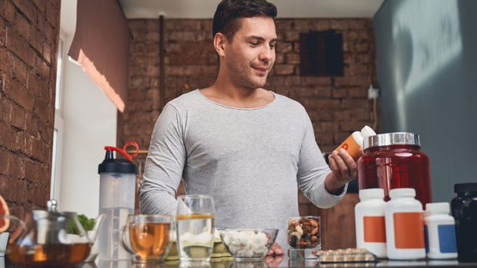 Waist-up portrait of a concentrated dark-haired male reading a label on a bottle of vitamins