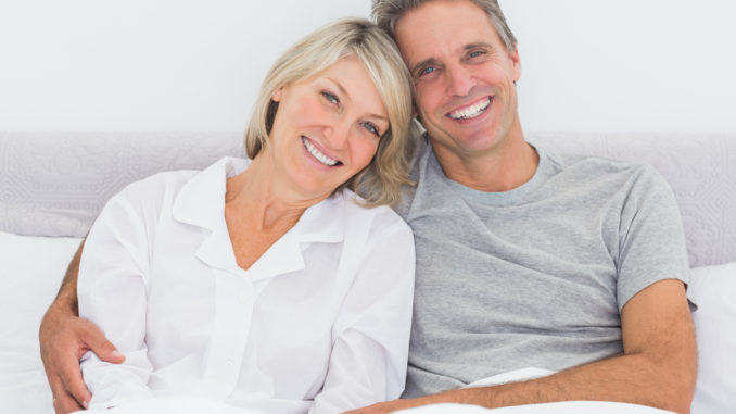 Happy couple in bed smiling at camera