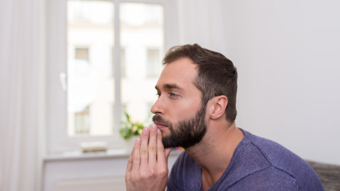 Worried bearded man sitting thinking with his clasped hands to his chin staring off into space in contemplation