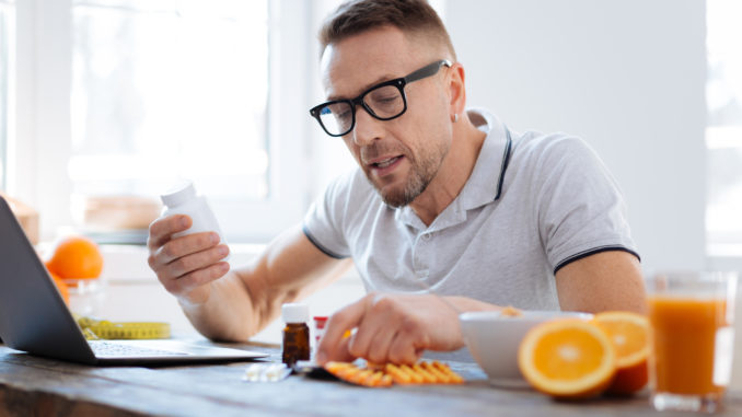 Biohack your life. Handsome progressive doubtful man deciding about biohacking supplements while sitting and improving his health