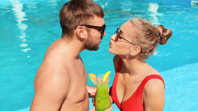 Young couple with refreshing cocktails near swimming pool at resort