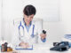 Smiling young doctor writing out a prescription for a bottle of medication as she sits in her office at the hospital