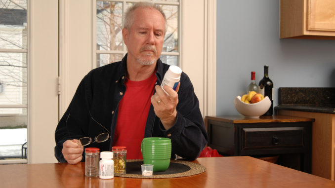 A man of retirement age reading the label of a vitamin bottle