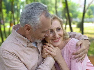 Happy senior couple embraces in park, men hugging woman