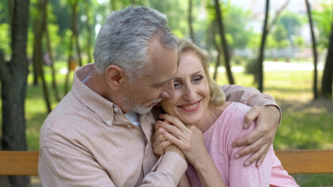 Happy senior couple embraces in park, men hugging woman