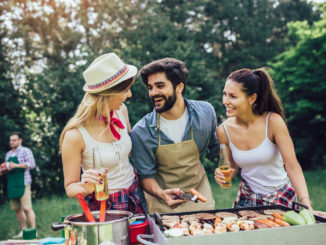 Happy friends grilling meat and enjoying barbecue party outdoors