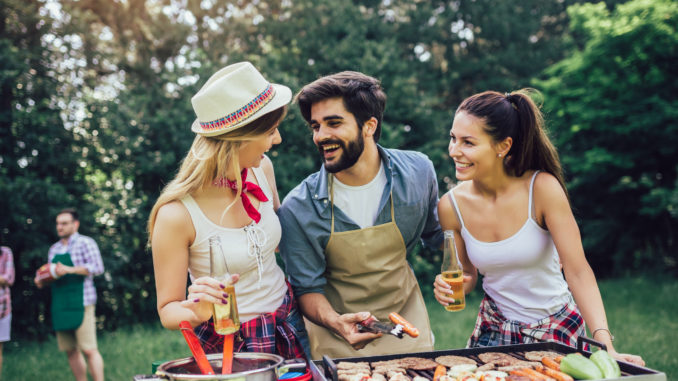 Happy friends grilling meat and enjoying barbecue party outdoors