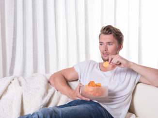 Young man sitting on couch and eating chips.