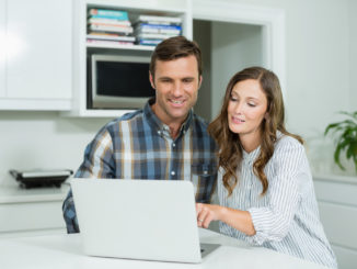 Happy couple interacting with each other while using laptop in living room at home