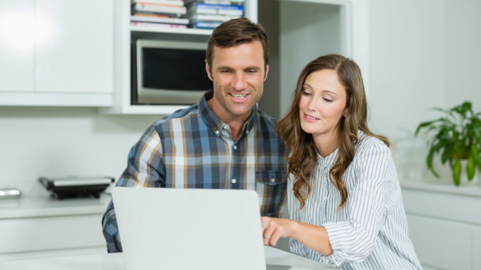 Happy couple interacting with each other while using laptop in living room at home