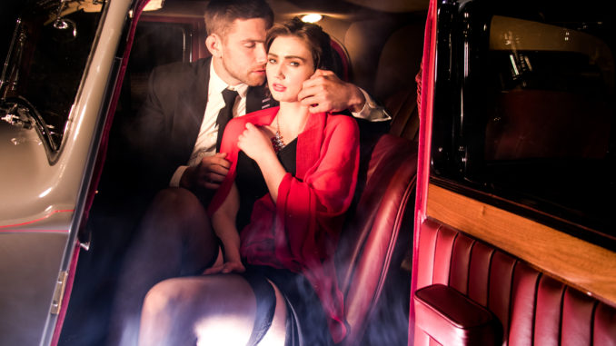 Good looking couple, handsome men in suit, beatiful women in red dress, touching, holding each other passionately in vintage car