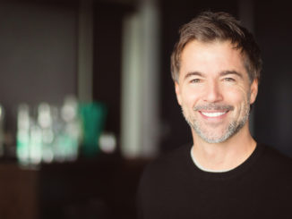 A handsome smiling middle-aged man with a short grey beard and brown hair.