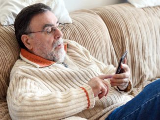 Elderly Man Using Cellphone Sitting On Sofa At Home