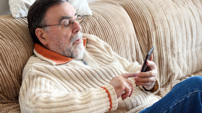 Elderly Man Using Cellphone Sitting On Sofa At Home