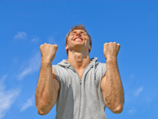 The winner. Happy energetic young man on blue sky background.