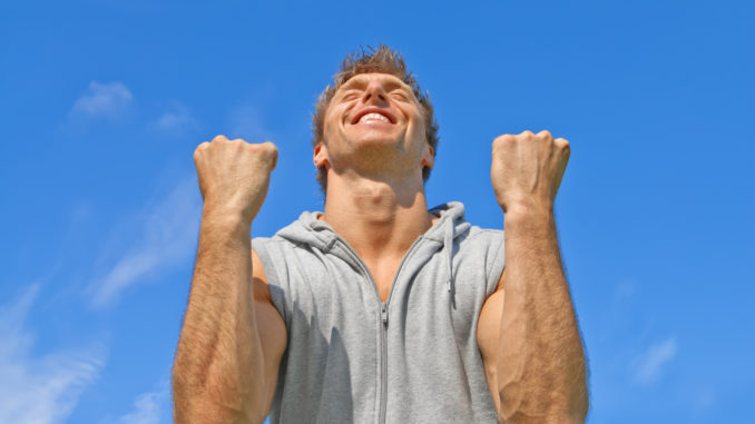 The winner. Happy energetic young man on blue sky background.