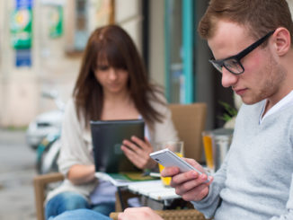 Man with cell phone and the women with the iPad sitting in a café. Secluded alley in a background.