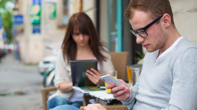 Man with cell phone and the women with the iPad sitting in a café. Secluded alley in a background.