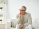Old age, problem and people concept - senior man in glasses thinking and sitting on sofa at home