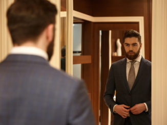 View from back of man in suit looking at the mirror while being in shop
