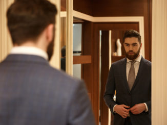 View from back of man in suit looking at the mirror while being in shop