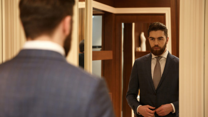 View from back of man in suit looking at the mirror while being in shop
