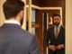 View from back of man in suit looking at the mirror while being in shop