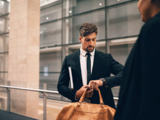 Young businessman at airport with bag looking at his watch. Business traveler at airport terminal checking time.