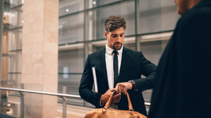 Young businessman at airport with bag looking at his watch. Business traveler at airport terminal checking time.