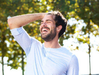 Portrait of happy young man smiling outdoors with hand in hair