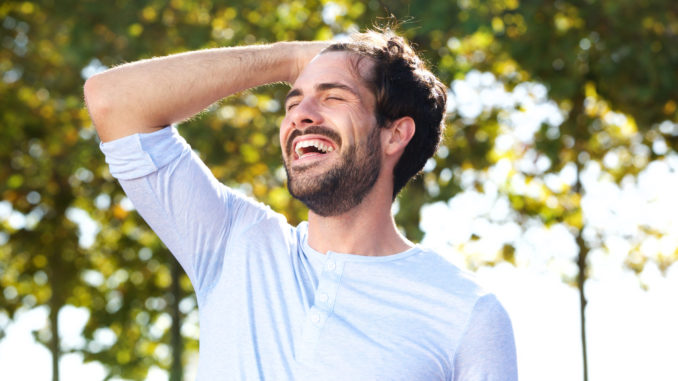 Portrait of happy young man smiling outdoors with hand in hair