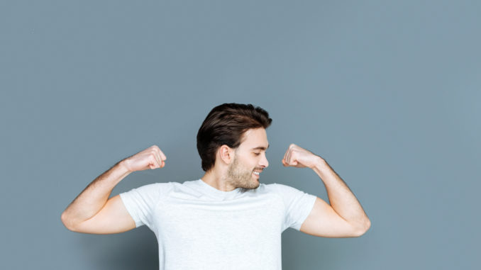 Strong body. Happy nice well built man smiling and looking at his muscles while feeling joyful about his strength