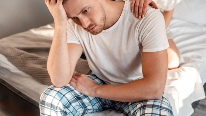 Young couple in the bed. Close-up of unhappy men in pajamas is sitting on the edge of bed, problem in the bedroom