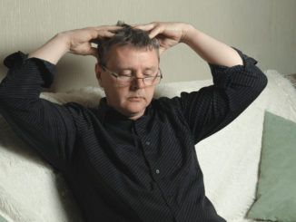 A man with glasses and a black shirt is massaging his head.