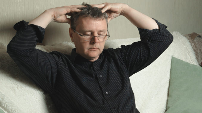 A man with glasses and a black shirt is massaging his head.