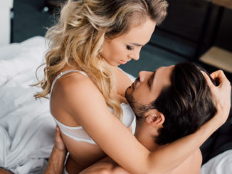 Passionate women touching hair of muscular men on bed