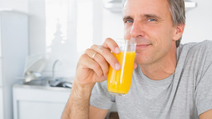 Happy man drinking orange juice in kitchen looking at camera