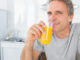 Happy man drinking orange juice in kitchen looking at camera
