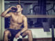Attractive athletic shirtless young man drinking protein shake from blender in gym